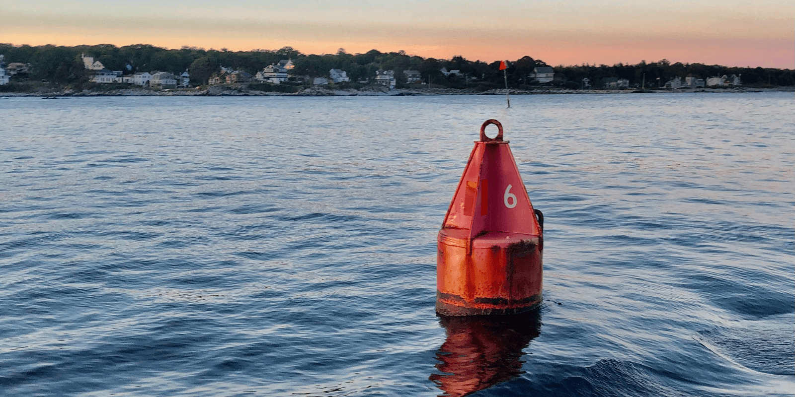 A red buoy floating in a large body of water with land in the background.